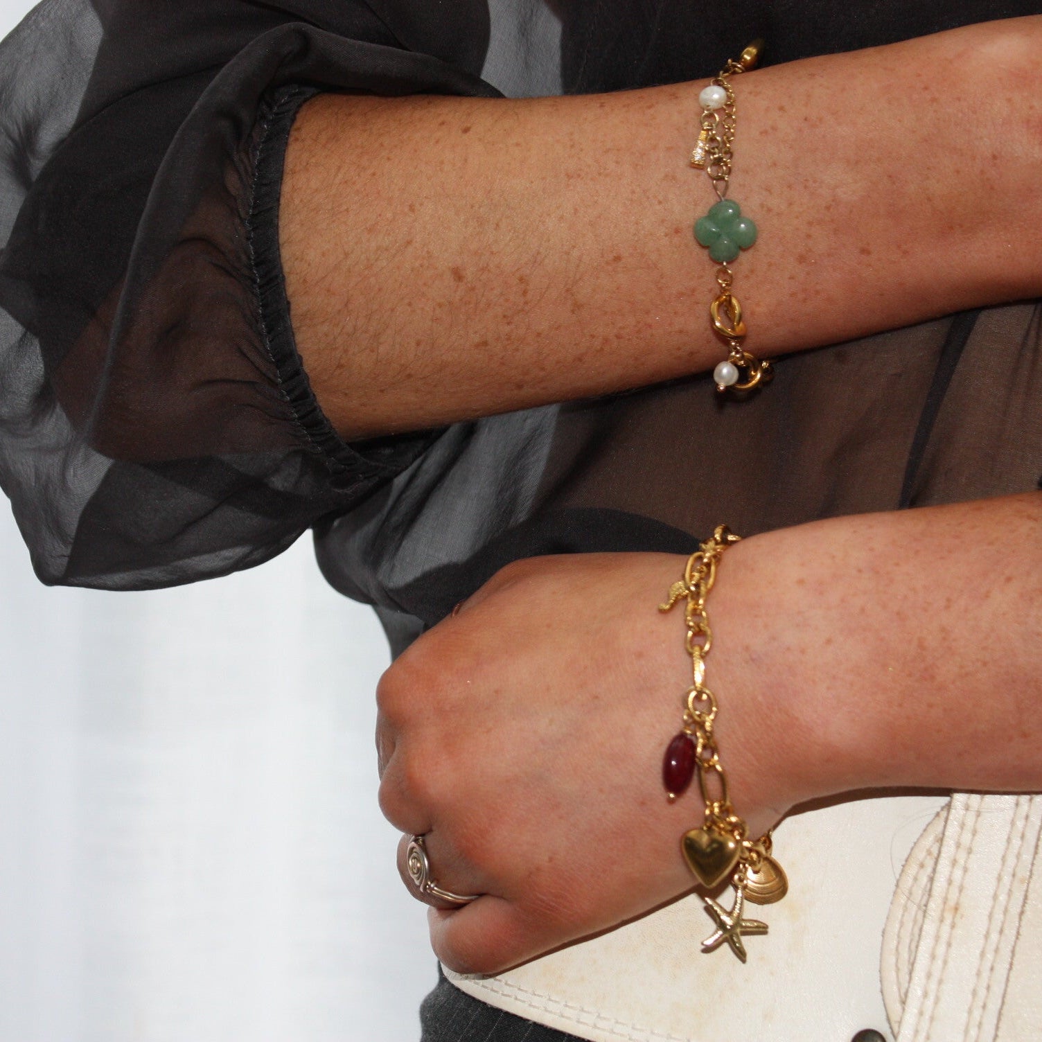 A stylish close-up of a model wearing an asymmetric charm bracelet adorned with green stones and gold charms, showcasing its elegant and versatile design.