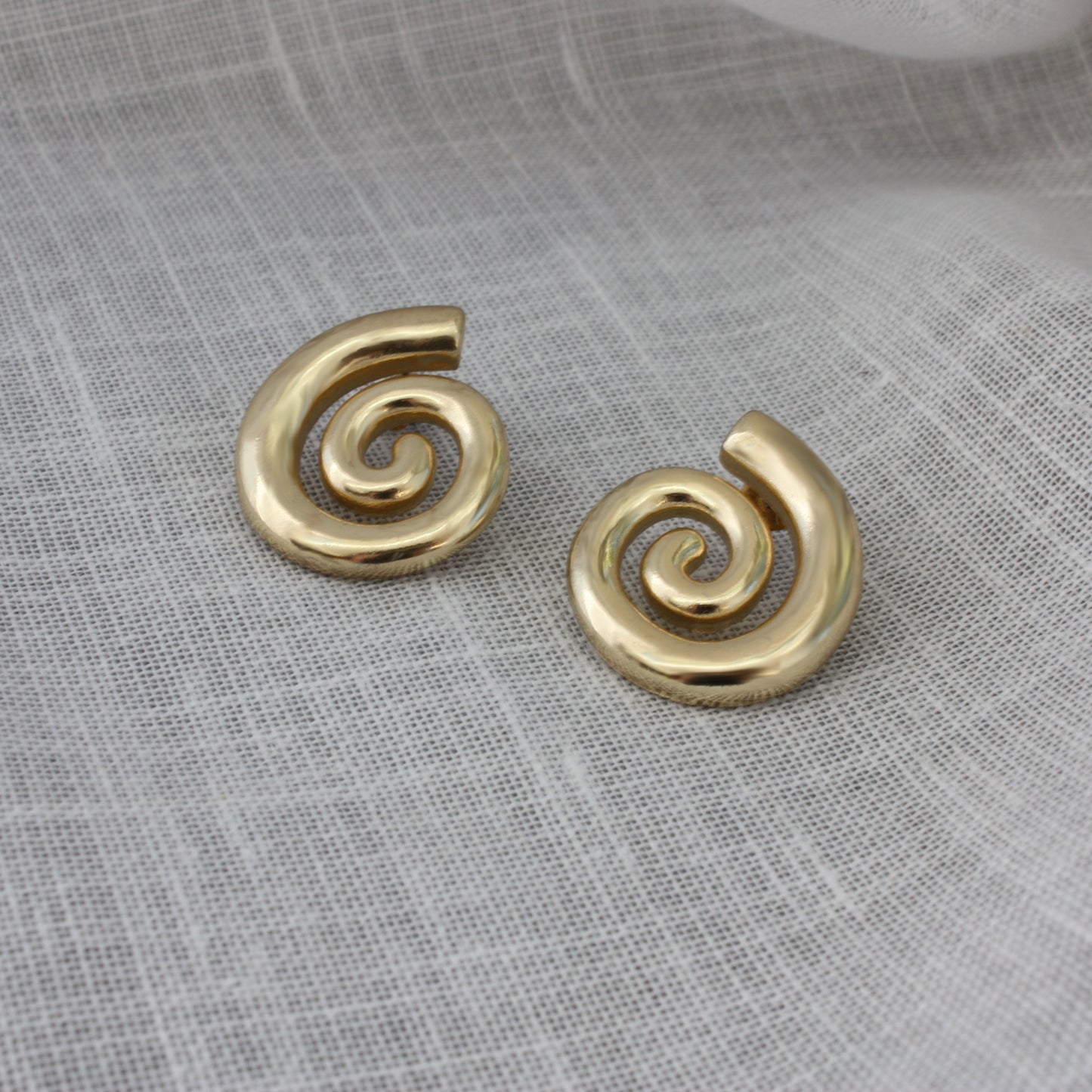 ÈRE Iris Earrings displayed on a textured surface, highlighting their elegant spiral shape. Ideal gold statement earrings for any outfit.
