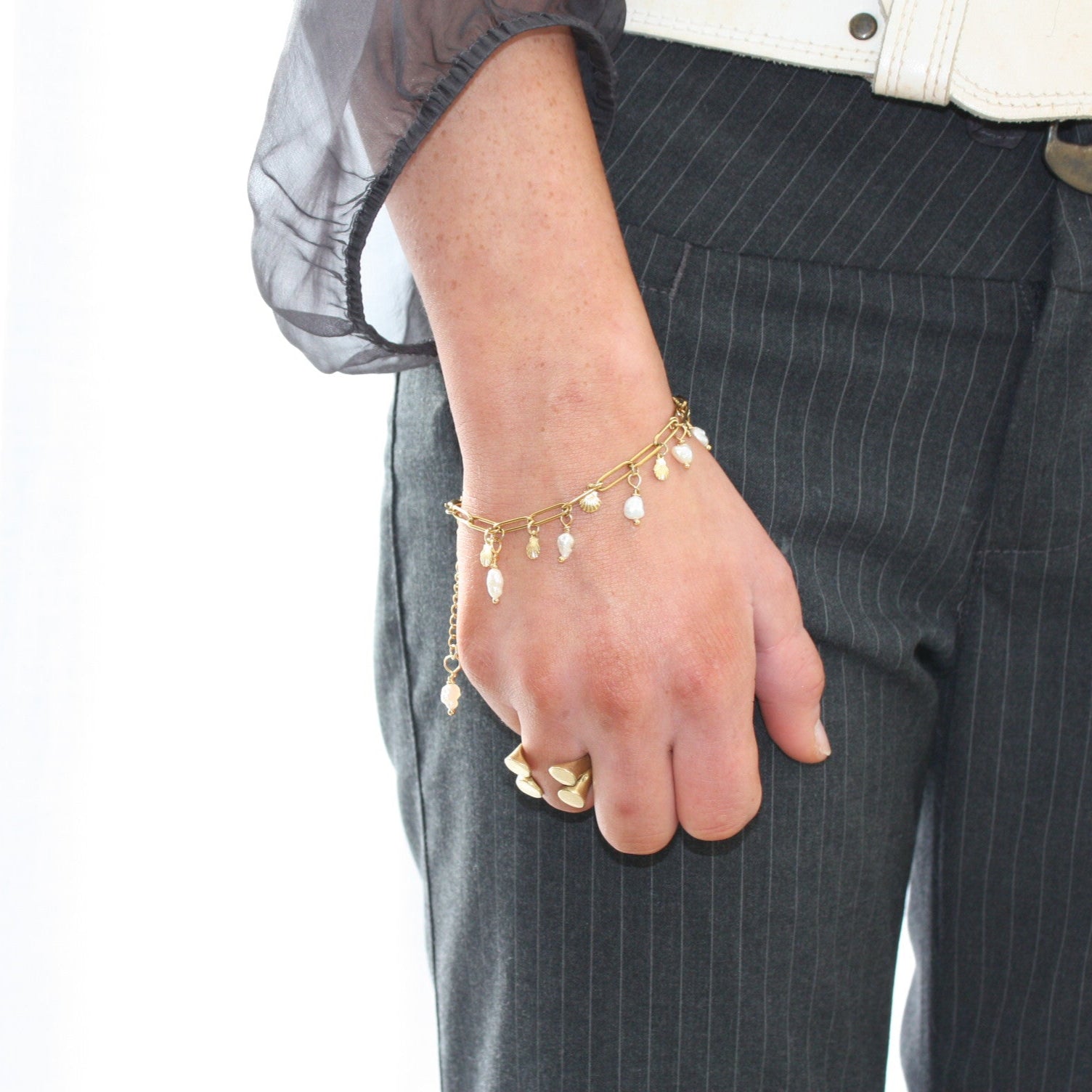 Close-up of a pearl charm bracelet on a model's wrist, highlighting the intricate seashell and pearl details.