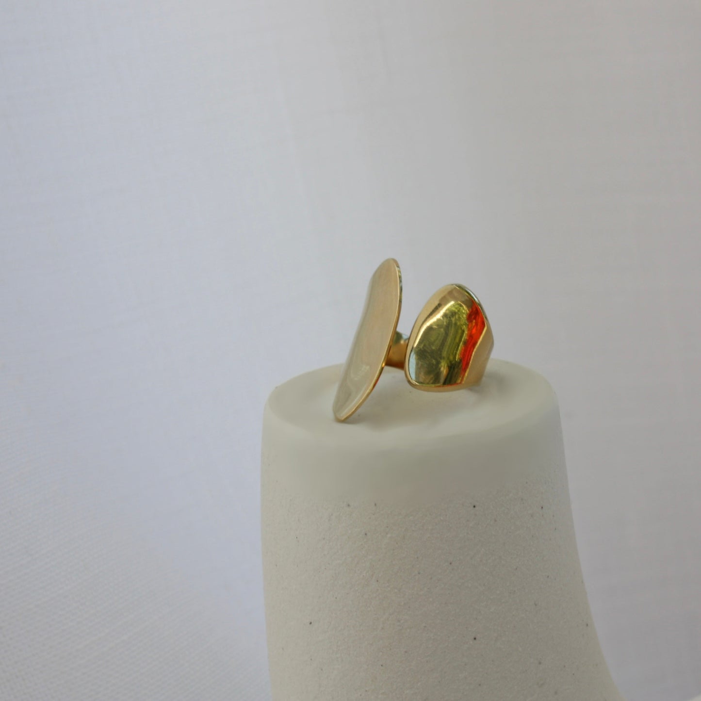 Stylized display of the Sloane Ring by ÈRE, highlighting its bold and sophisticated look. The adjustable gold ring is artistically positioned on a textured pedestal.