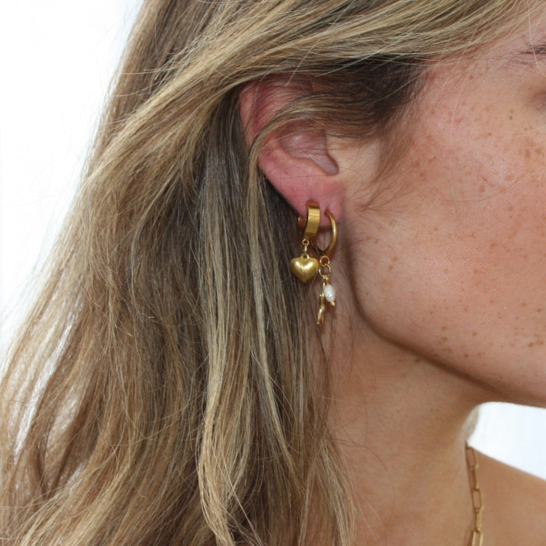 Close-up of a model wearing gold heart earrings, styled with additional jewellery for a trendy look.