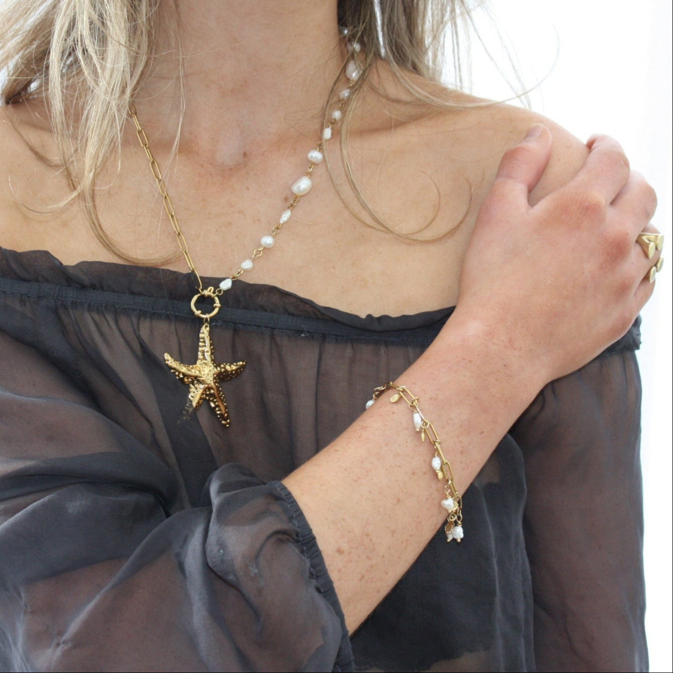 Woman wearing a pearl charm bracelet alongside a starfish necklace, embodying a chic beach-themed style.