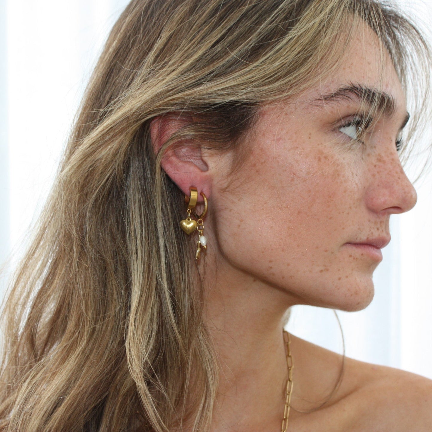 Side profile of a model showcasing gold heart earrings, capturing their graceful and fashionable appeal.