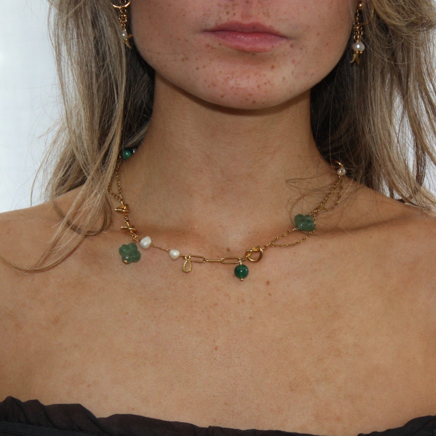 Close-up of the Asymmetric Charm Necklace draped elegantly, displaying its combination of gold, pearls, and natural green stones for a chic, handcrafted look.