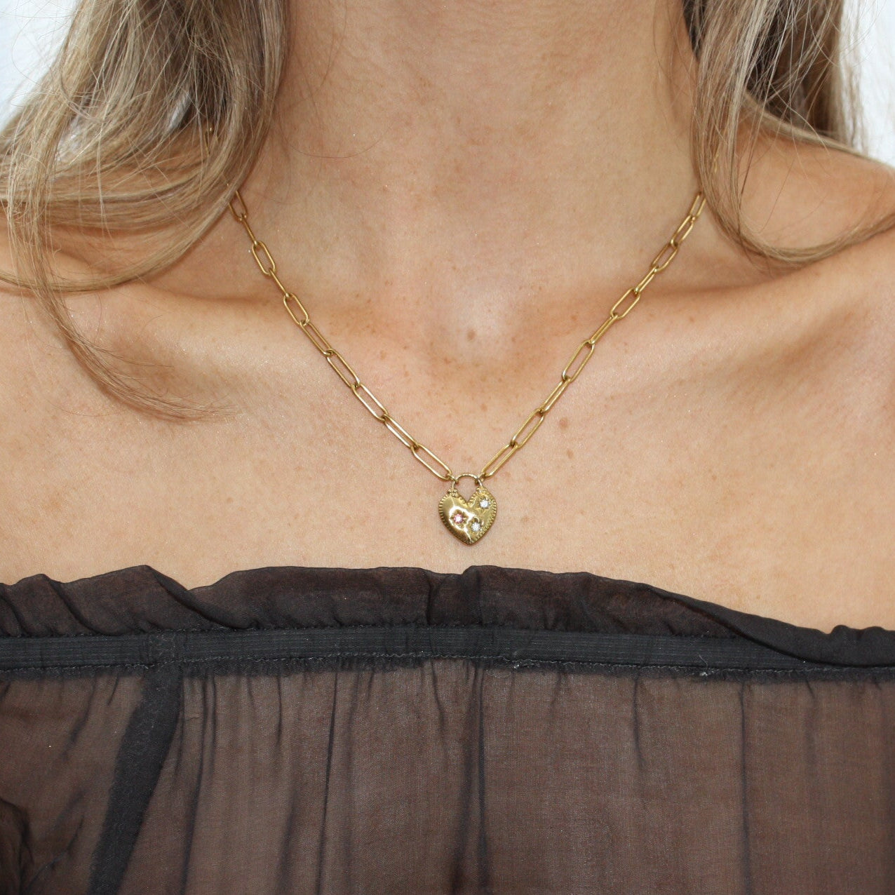 Model wearing a stunning heart necklace with a paperclip chain, showcasing a delicate heart pendant adorned with sparkling stones.