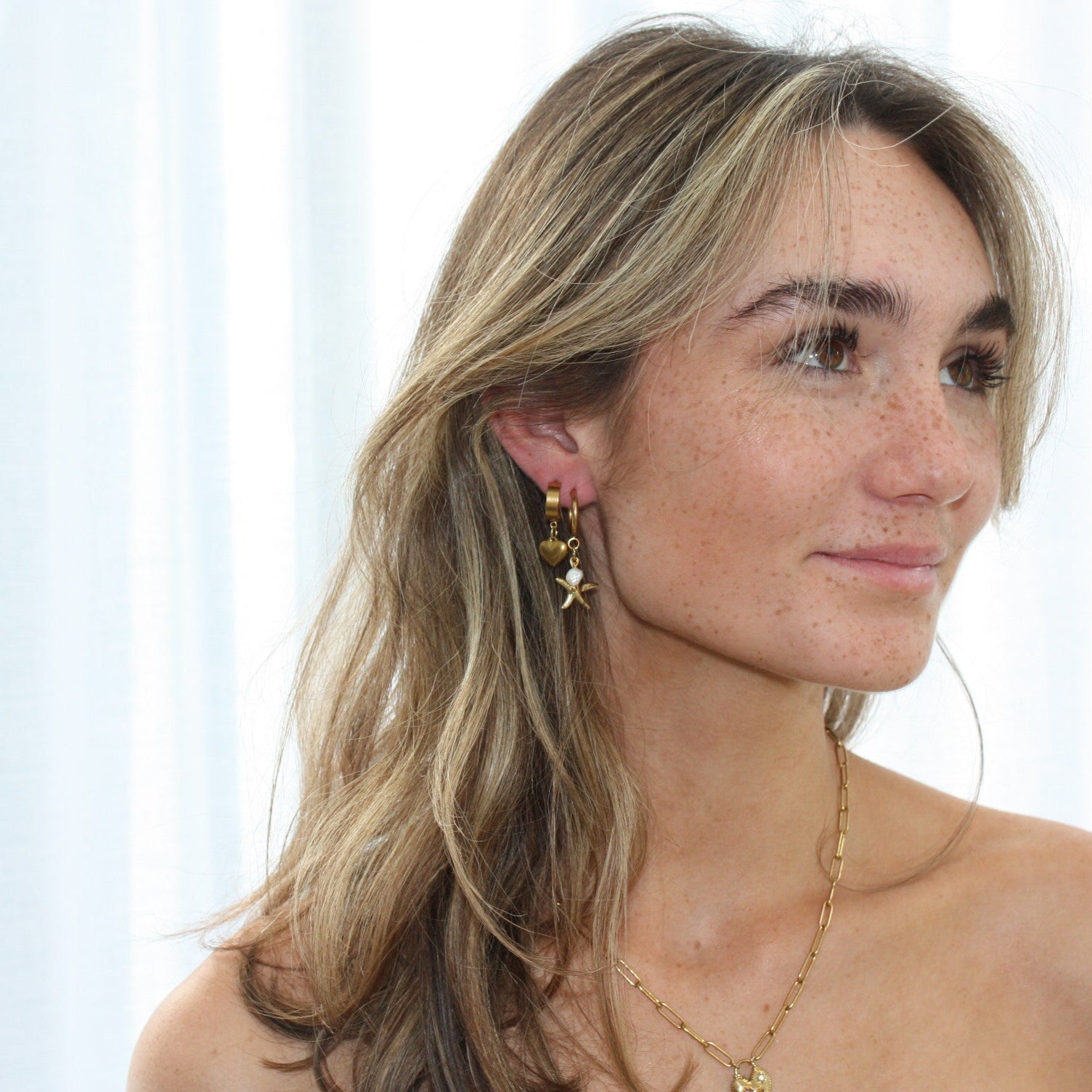 Side view of a model adorned with starfish hoops paired with other earrings, highlighting the unique starfish and pearl design.