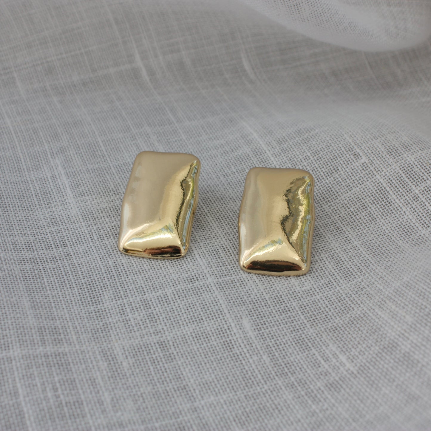 Elegant Harper Earrings from ÈRE displayed on a soft fabric, representing modern gold statement earrings with a shiny finish.