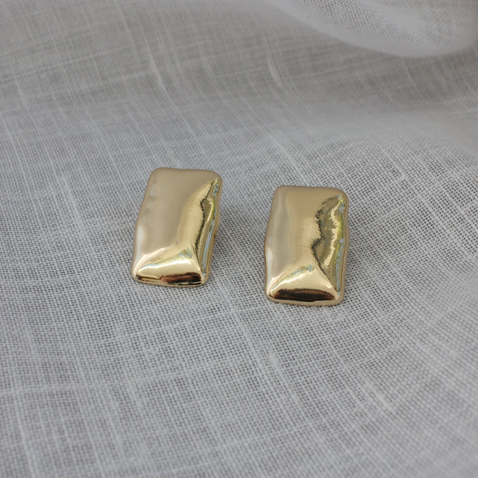 Elegant Harper Earrings from ÈRE displayed on a soft fabric, representing modern gold statement earrings with a shiny finish.