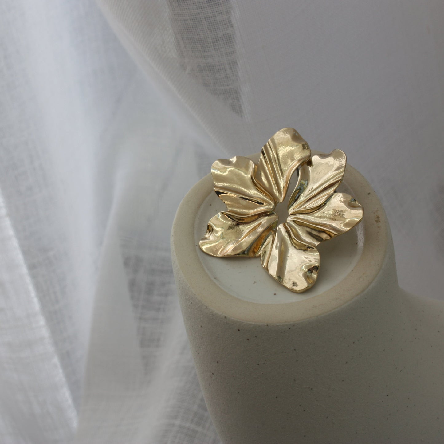 Faye Earrings by ÈRE placed on a minimalist display, showcasing their exquisite floral statement earrings design in gold.