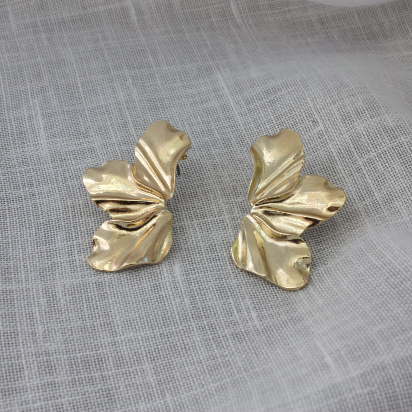 Close-up of Faye Earrings by ÈRE, beautifully crafted floral statement earrings in 18k gold plating on a soft fabric background.
