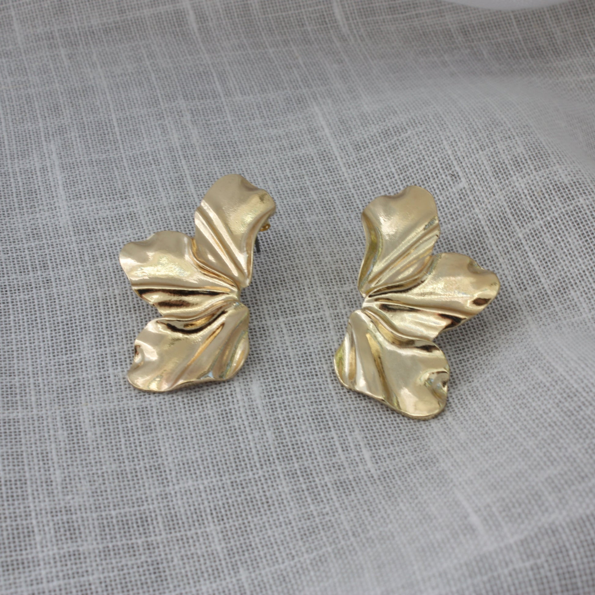 Close-up of Faye Earrings by ÈRE, beautifully crafted floral statement earrings in 18k gold plating on a soft fabric background.