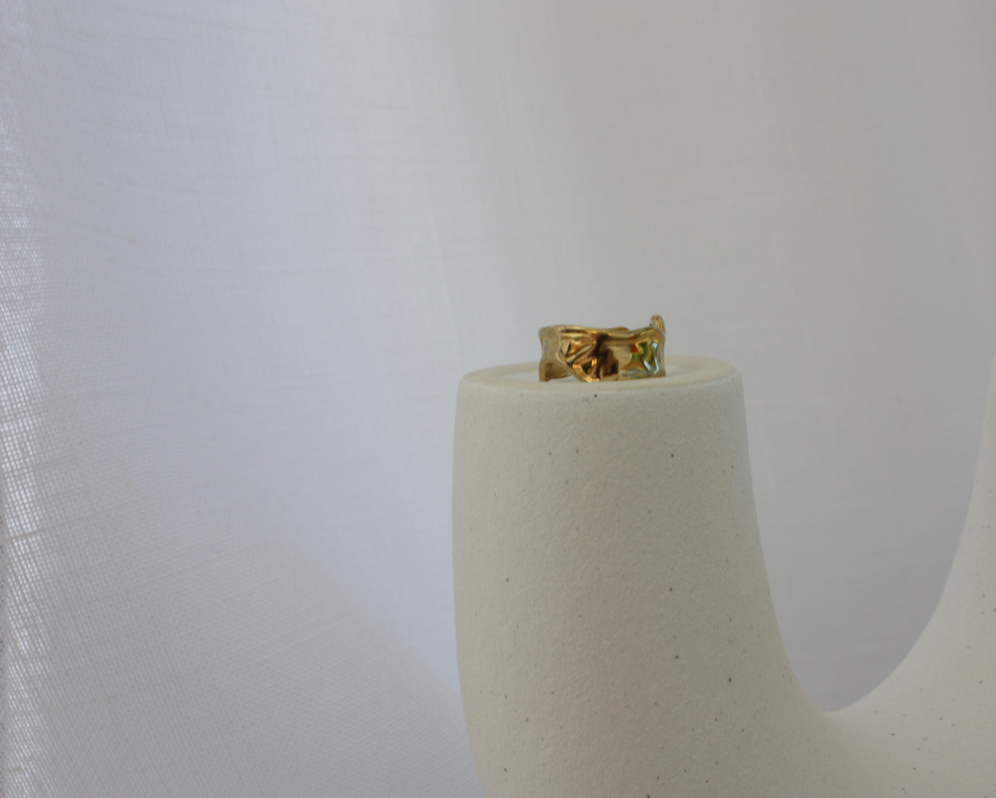 The Aurora Ring by ÈRE elegantly displayed on a minimalistic pedestal, highlighting its vintage-inspired asymmetrical gold ring design made with 18k gold plating.