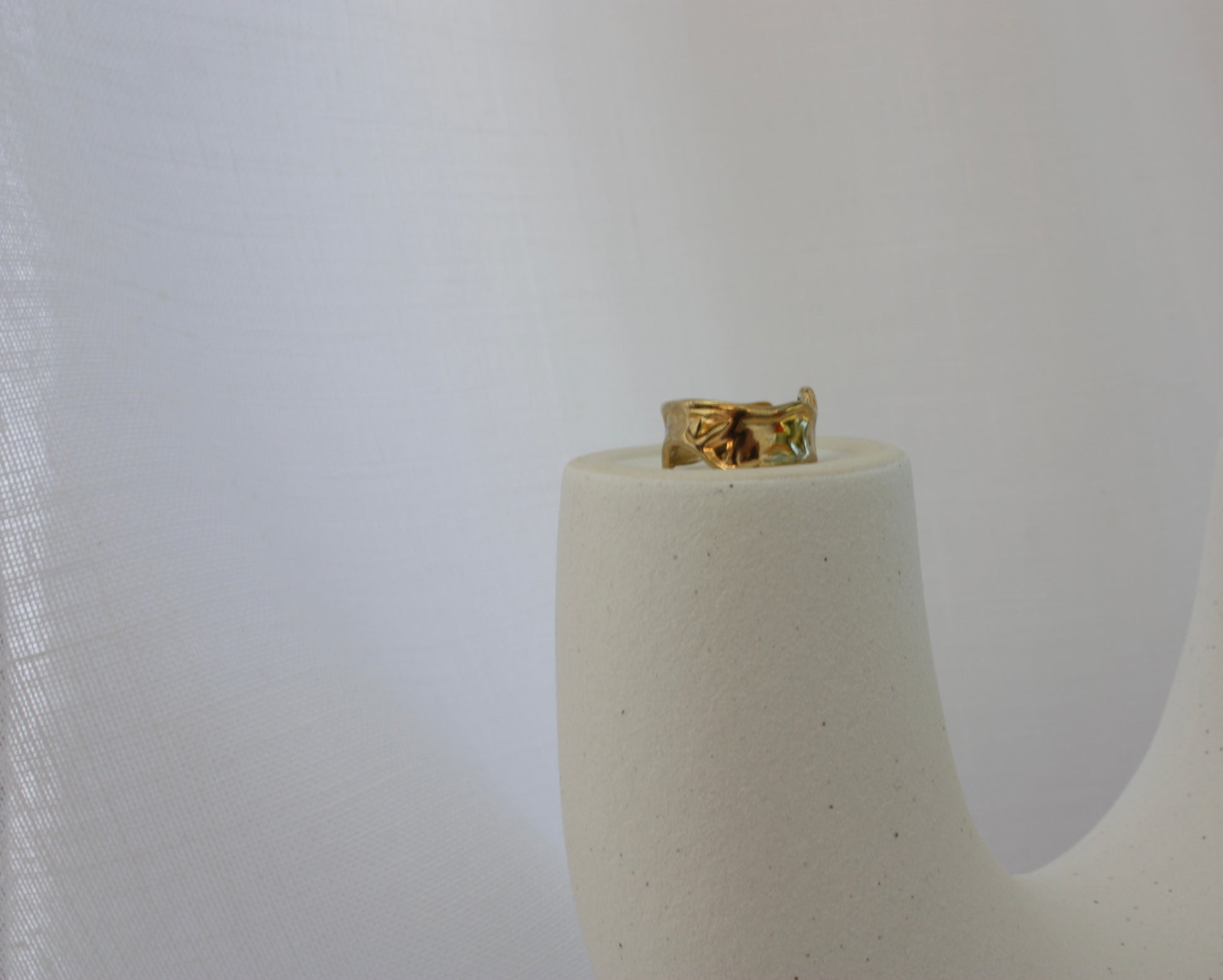 The Aurora Ring by ÈRE elegantly displayed on a minimalistic pedestal, highlighting its vintage-inspired asymmetrical gold ring design made with 18k gold plating.