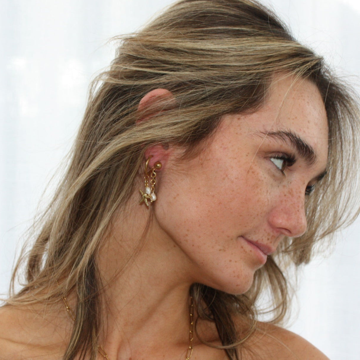 Close-up of a model wearing pearl earrings, showcasing their elegant design featuring natural freshwater pearls and gold accents, highlighting a trendy earring stack look.