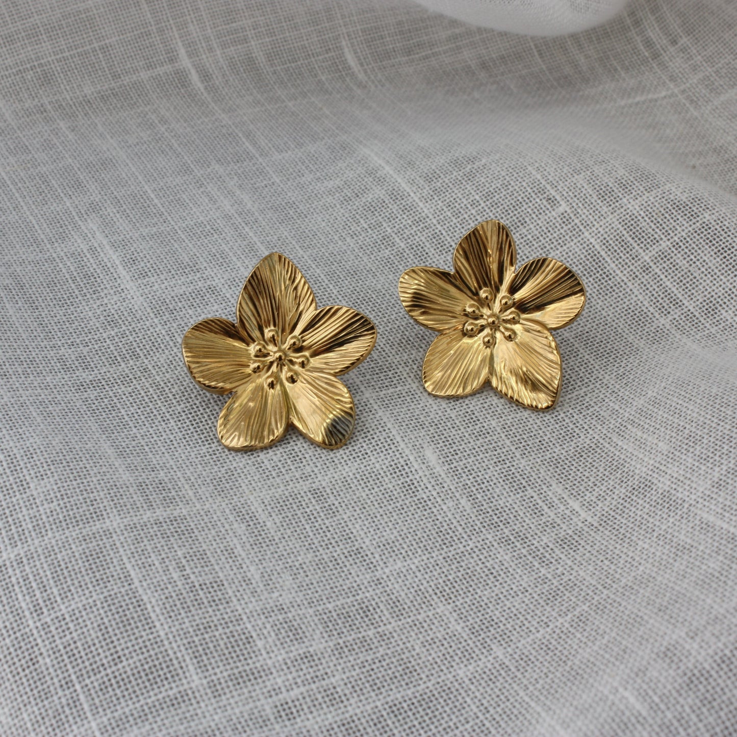 Stylish Fleur Earrings by ÈRE displayed on a soft fabric background, emphasizing their gold sheen and floral motif. Ideal flower statement earrings for a chic look.