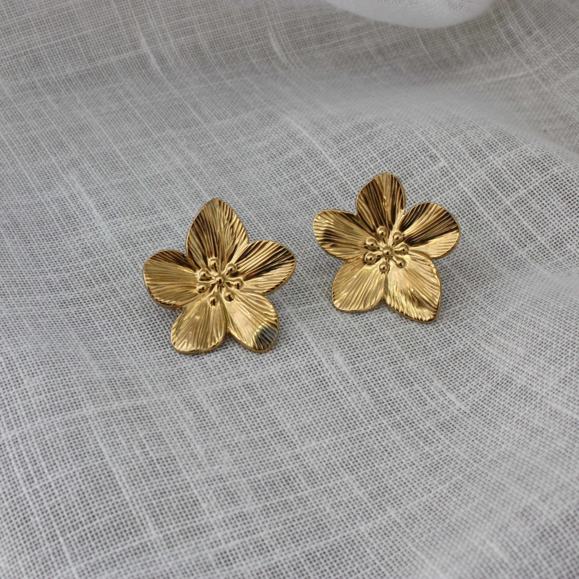 Stylish Fleur Earrings by ÈRE displayed on a soft fabric background, emphasizing their gold sheen and floral motif. Ideal flower statement earrings for a chic look.