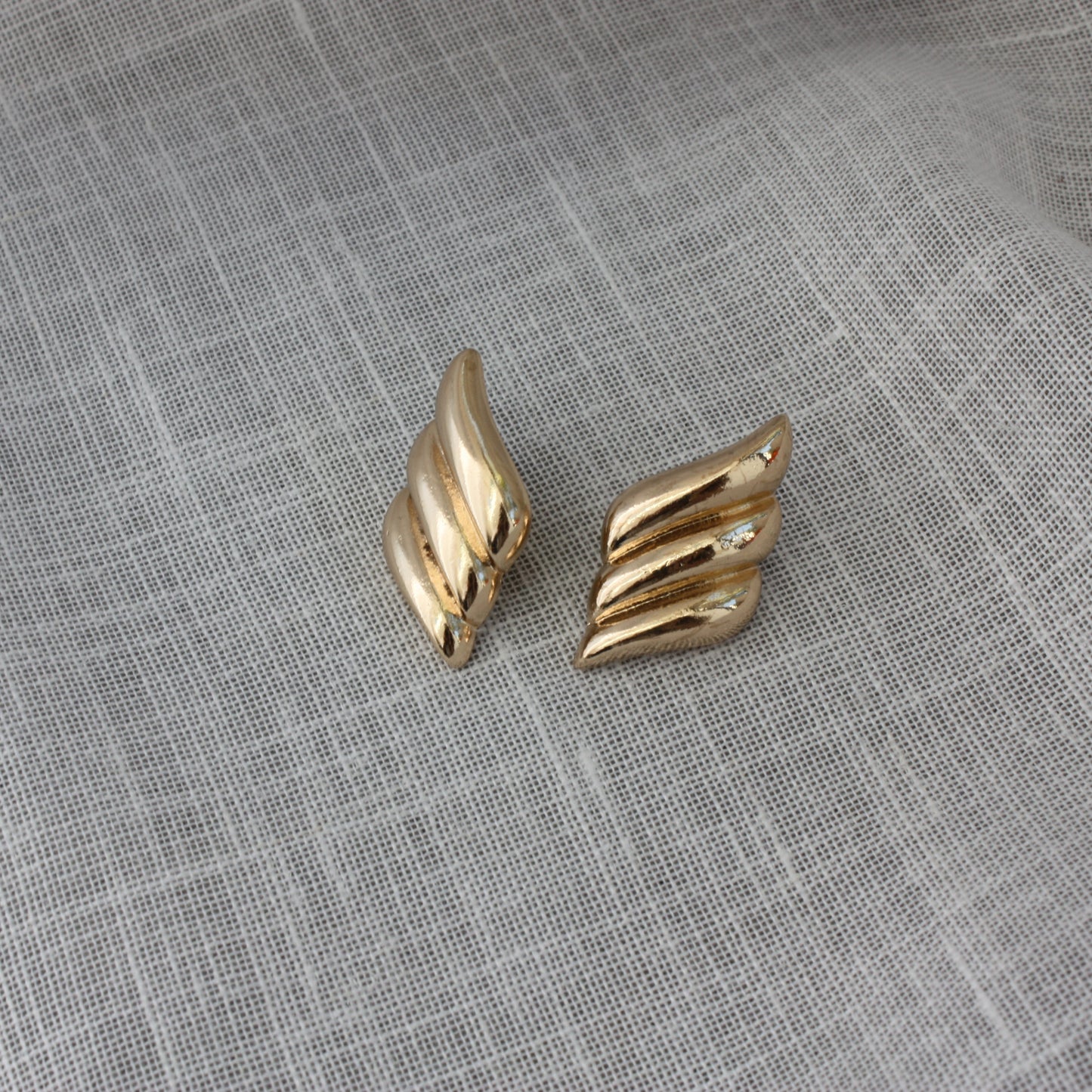 Stylish Paloma Earrings by ÈRE displayed on a soft textured surface, showcasing their intricate wing-inspired design as standout gold statement earrings.
