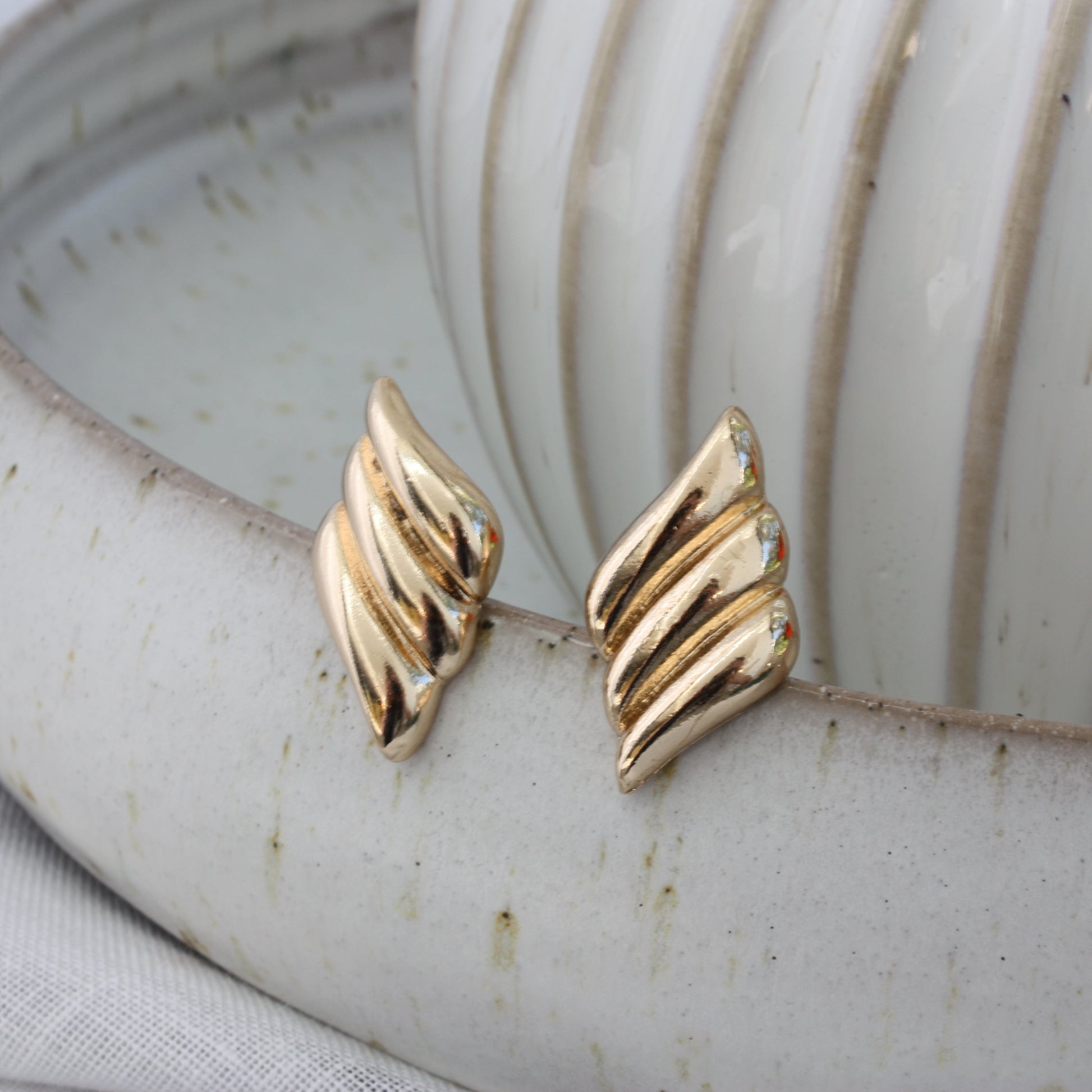 Chic Paloma Earrings by ÈRE positioned artfully beside a minimalist ceramic bowl, highlighting the unique aesthetic of these gold statement earrings.